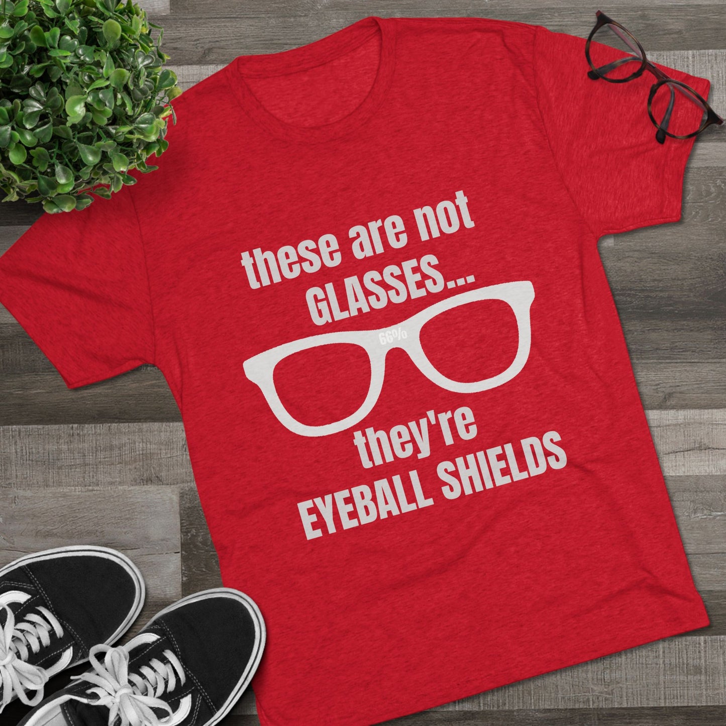 Light heather tri-blend tee flat-laid, printed with glasses graphic and text ‘these are not GLASSES... they’re EYEBALL SHIELDS.