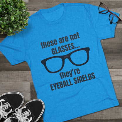 Light heather tri-blend tee flat-laid, printed with black glasses graphic and text ‘these are not GLASSES... they’re EYEBALL SHIELDS.