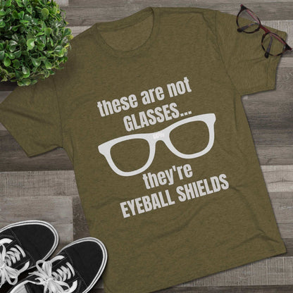 Light heather tri-blend tee flat-laid, printed with glasses graphic and text ‘these are not GLASSES... they’re EYEBALL SHIELDS.