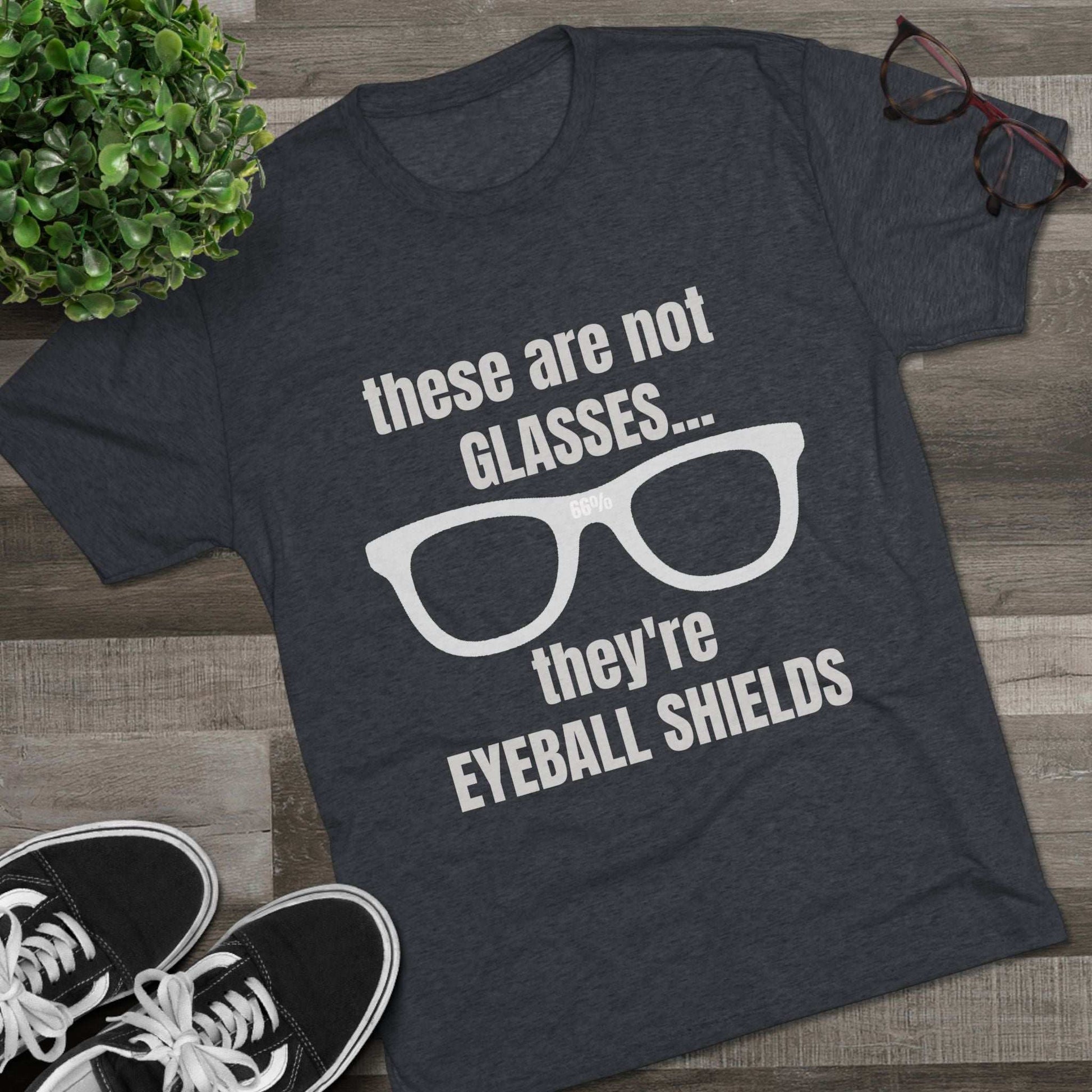 Light heather tri-blend tee flat-laid, printed with glasses graphic and text ‘these are not GLASSES... they’re EYEBALL SHIELDS.