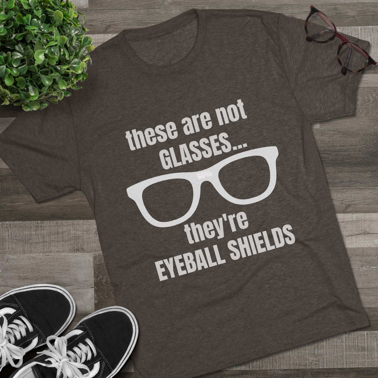 Light heather tri-blend tee flat-laid, printed with glasses graphic and text ‘these are not GLASSES... they’re EYEBALL SHIELDS.