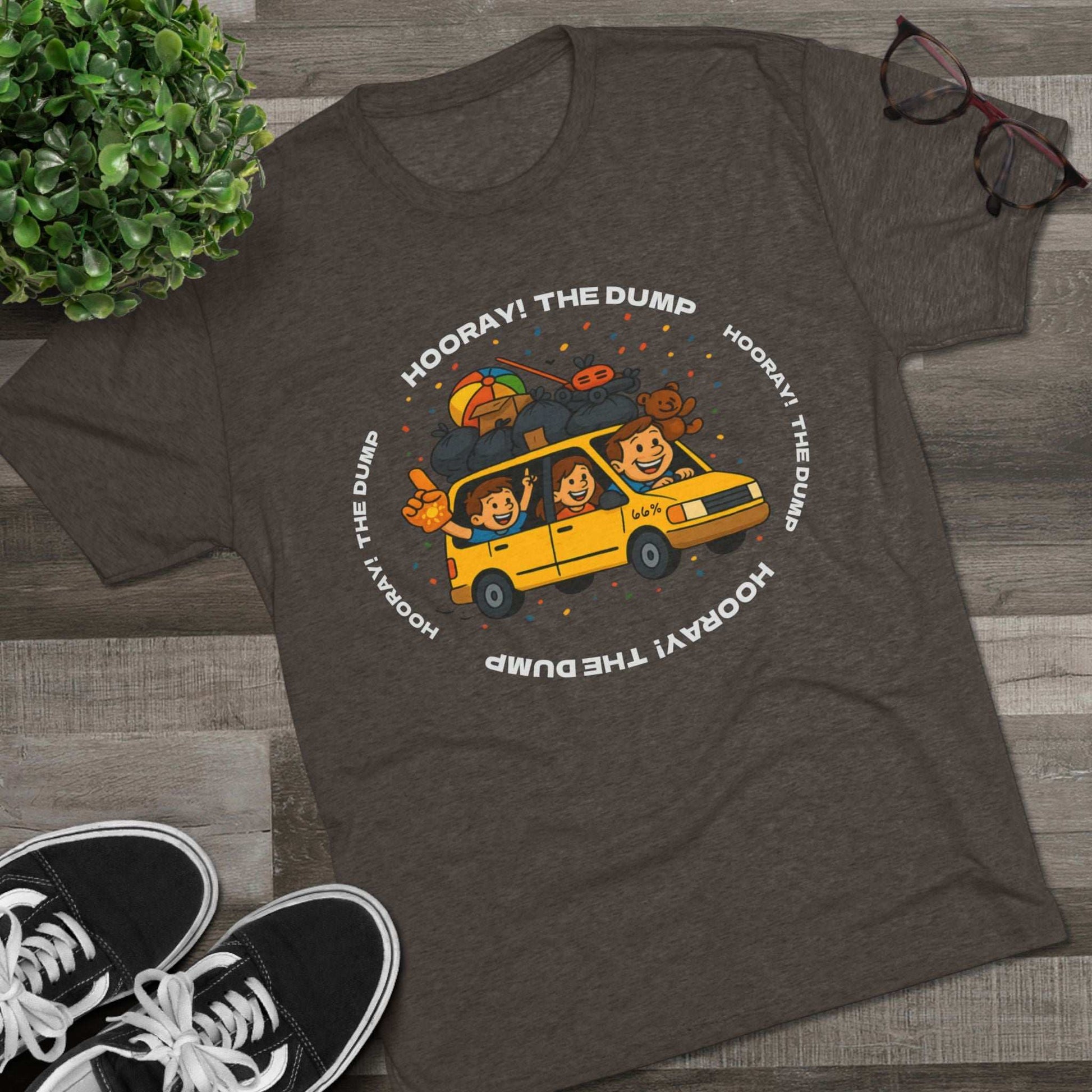 Cartoon yellow “66%” minivan T-shirt design with roof piled high in trash bags, lawnmower and beach ball, plus a dad driving and two excited kids waving with confetti.