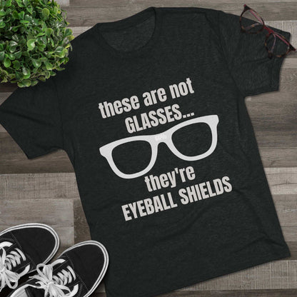 Light heather tri-blend tee flat-laid, printed with glasses graphic and text ‘these are not GLASSES... they’re EYEBALL SHIELDS.