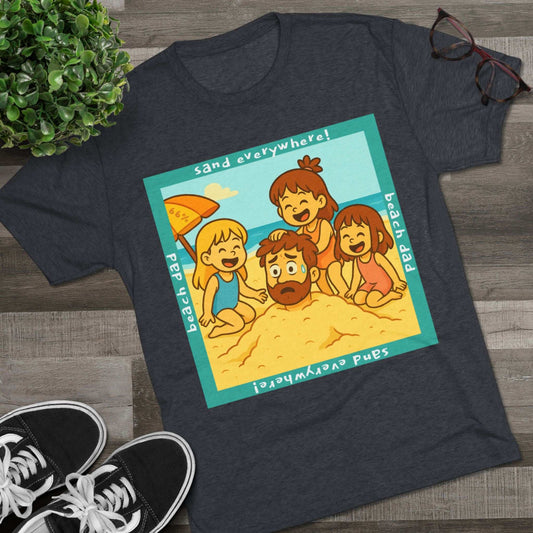 “Beach Dad Buried 66% Tri-Blend Tee — graphic tee flat-lay, cartoon dad sand-buried under umbrella, three kids playing, teal ‘sand everywhere!’ square border, ‘beach dad’ text, unisex casual style.
