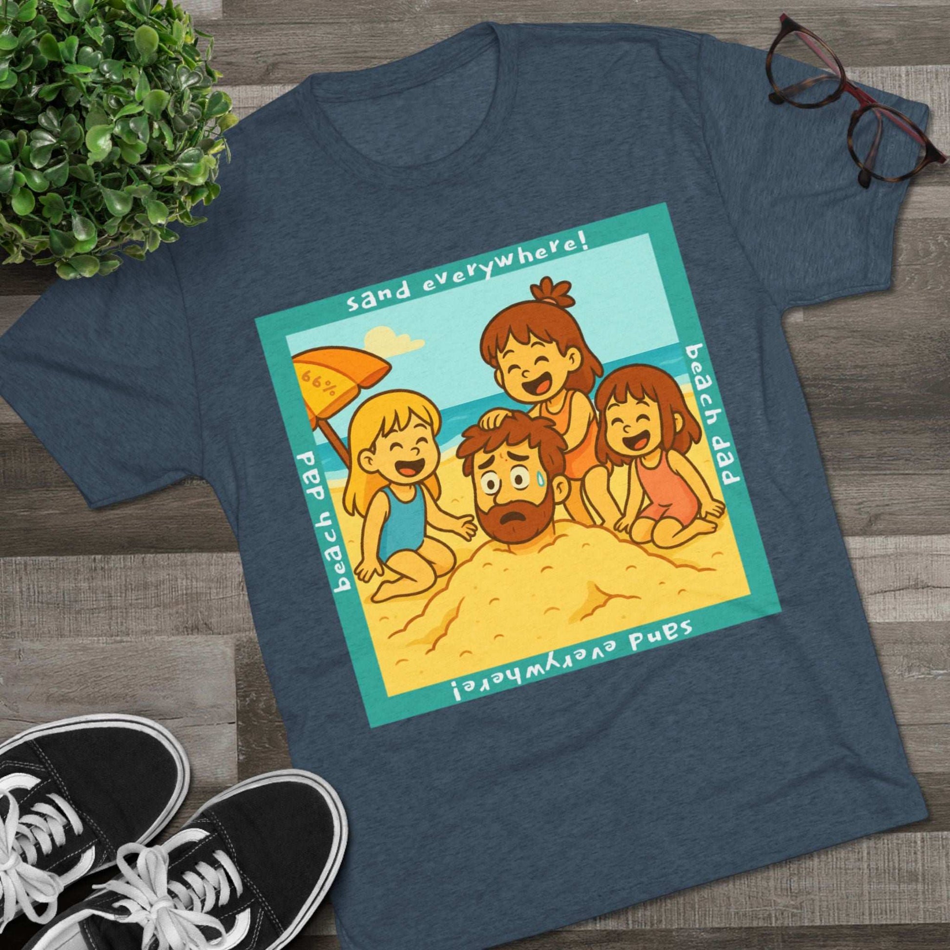 “Beach Dad Buried 66% Tri-Blend Tee — graphic tee flat-lay, cartoon dad sand-buried under umbrella, three kids playing, teal ‘sand everywhere!’ square border, ‘beach dad’ text, unisex casual style.