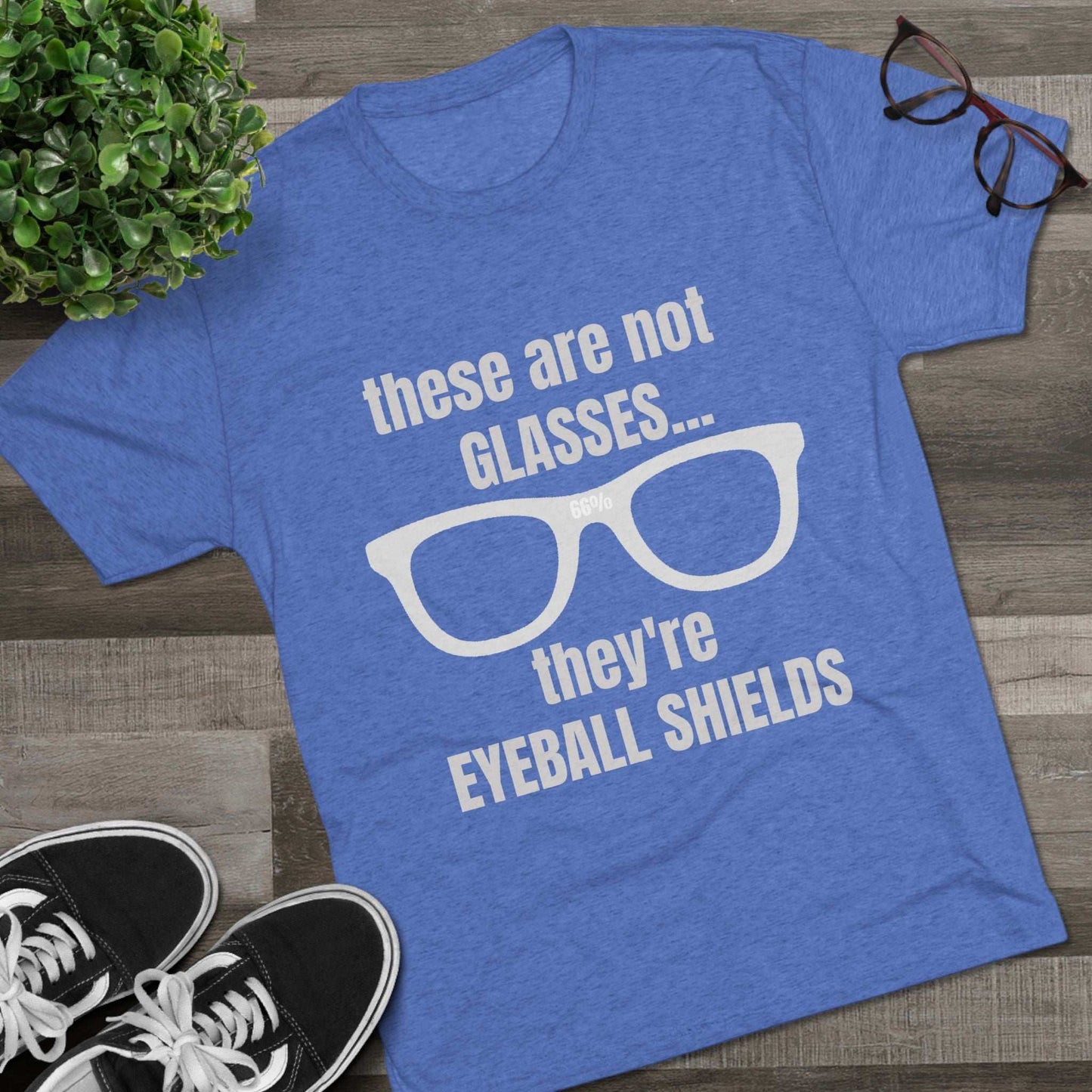 Light heather tri-blend tee flat-laid, printed with glasses graphic and text ‘these are not GLASSES... they’re EYEBALL SHIELDS.