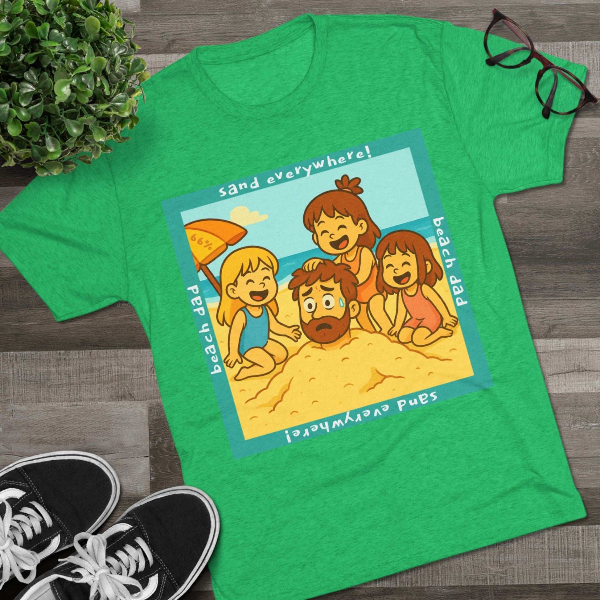 “Beach Dad Buried 66% Tri-Blend Tee — graphic tee flat-lay, cartoon dad sand-buried under umbrella, three kids playing, teal ‘sand everywhere!’ square border, ‘beach dad’ text, unisex casual style.